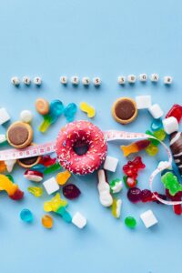 Various candies and desserts which may be detrimental to blood sugar health, a tape measure, and beads that spell out "eat less sugar"